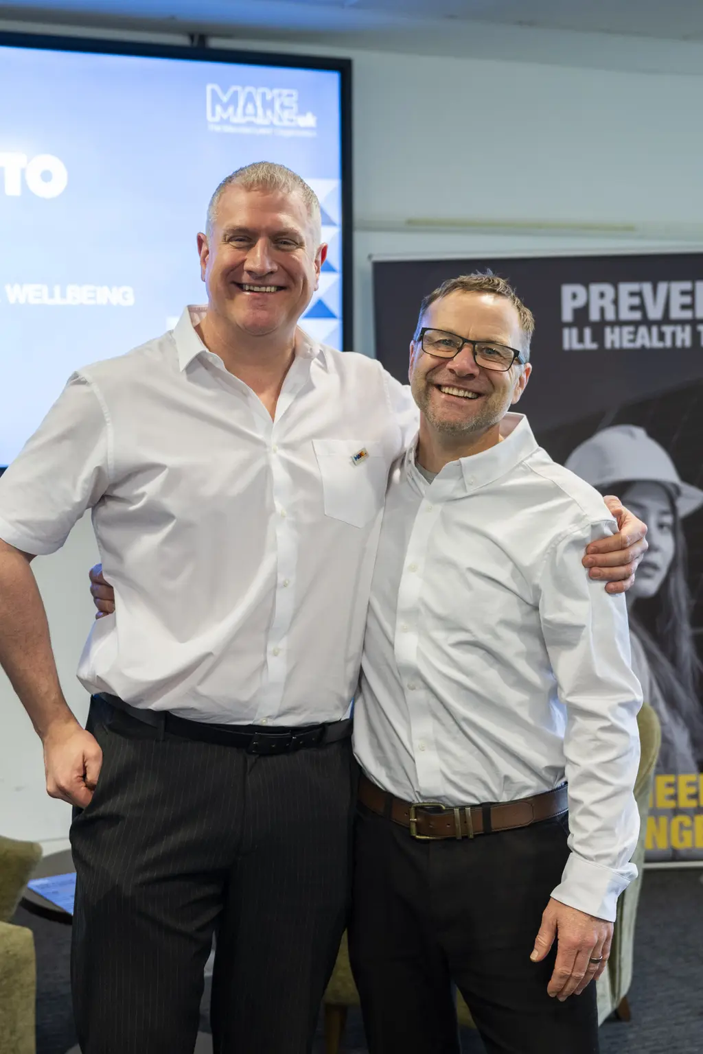 Two men stand next to a poster with the words "From Intent to Impact".