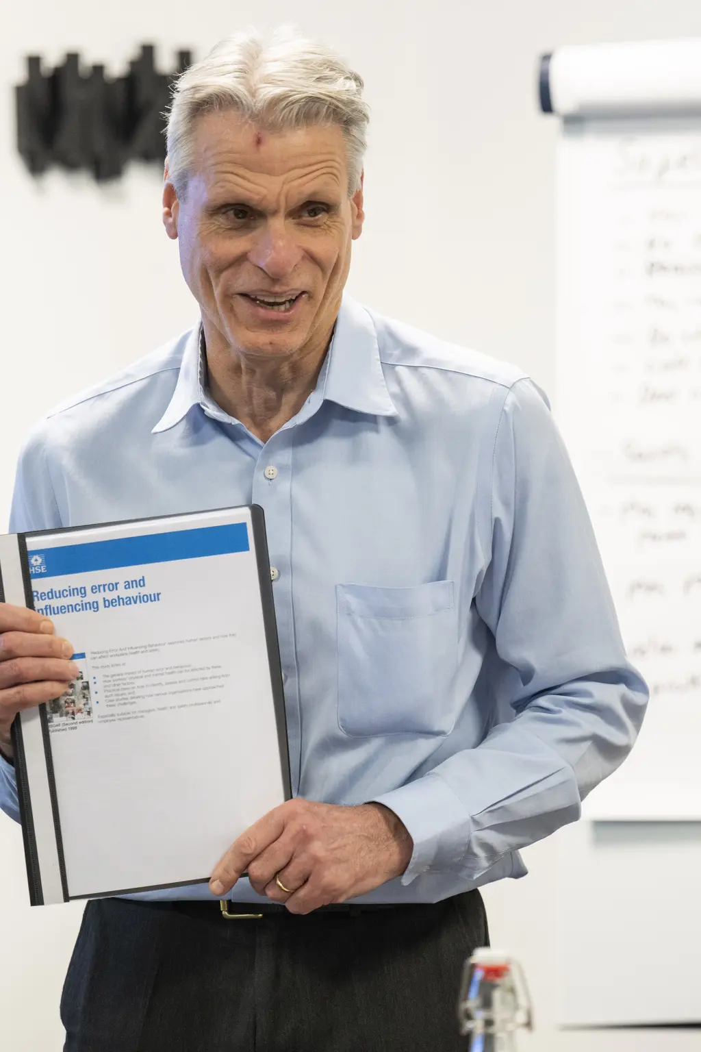 A man in a blue shirt holding a certificate in a classroom.