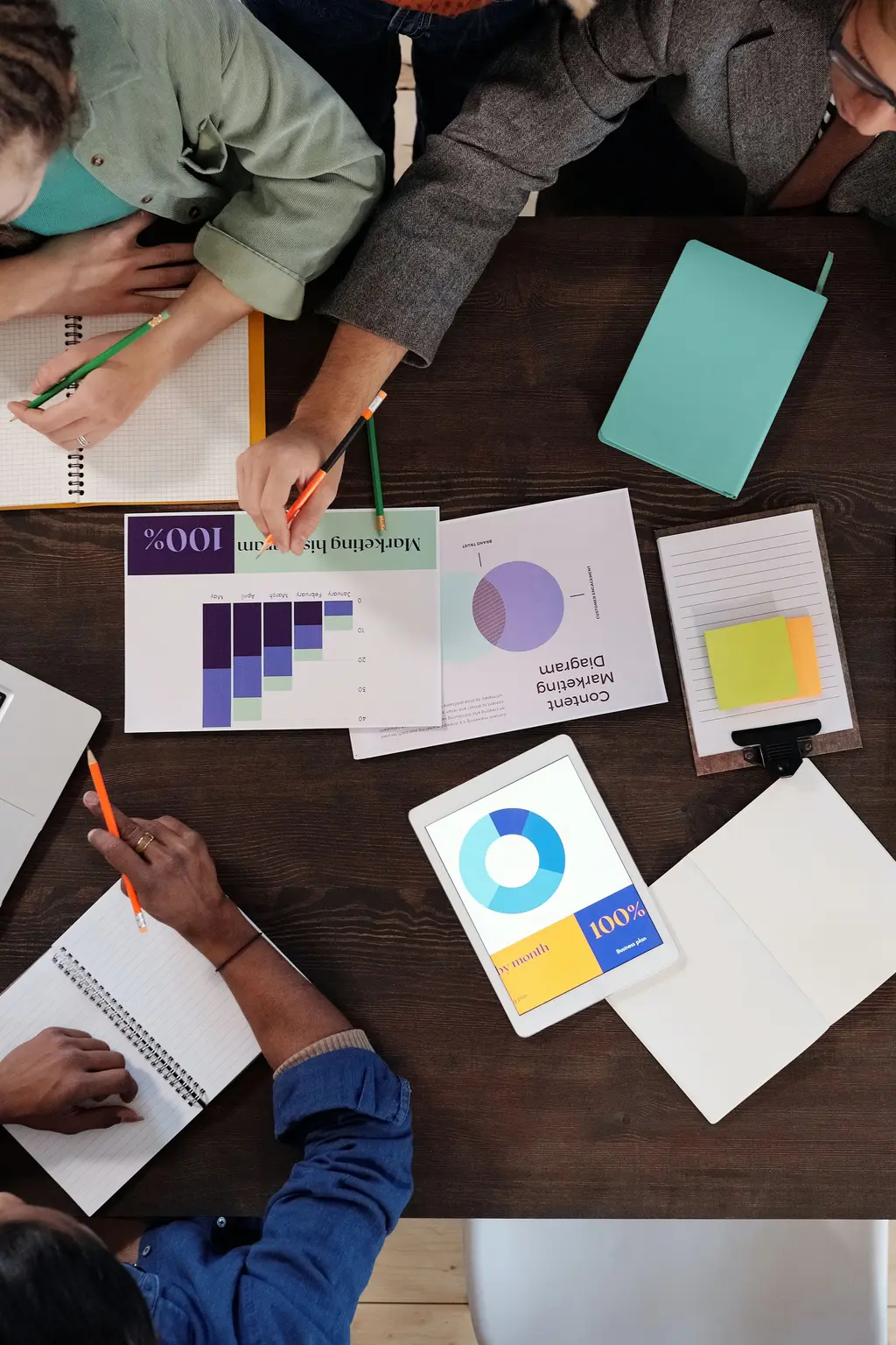 birds-eye view of people working at a desk with laptop and notepads
