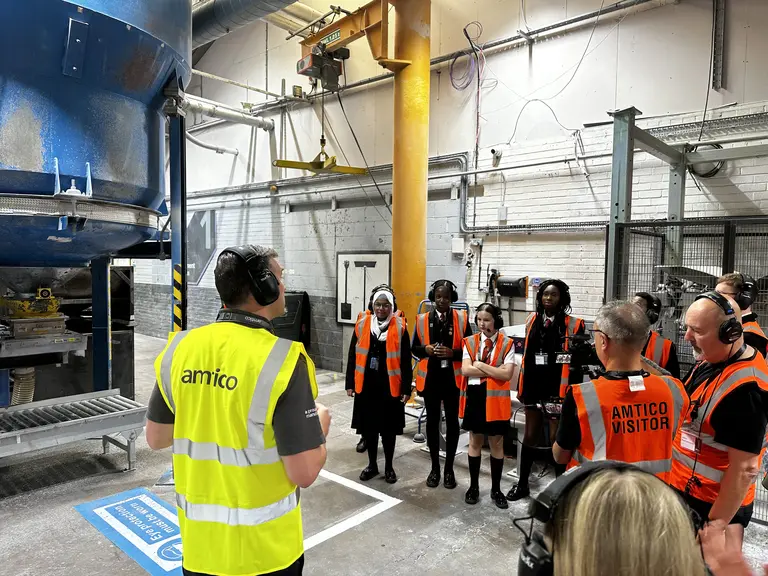 A group of people in reflective vests standing around in a factory for NMD 2025.