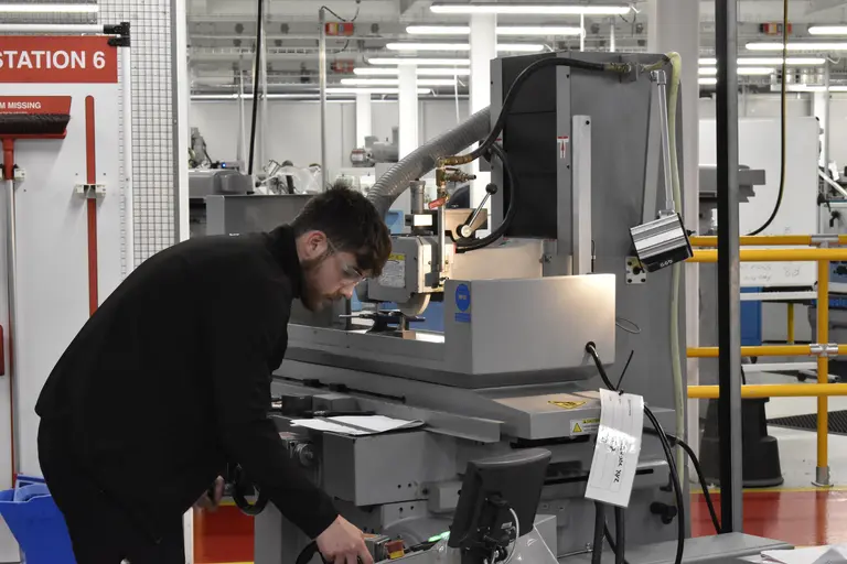 A man with safety goggles in a factory examining a machine.
