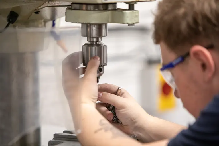A man in a blue shirt is working on a machine with tools.