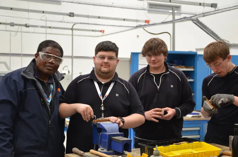 Four people in a shop with tools in front of them