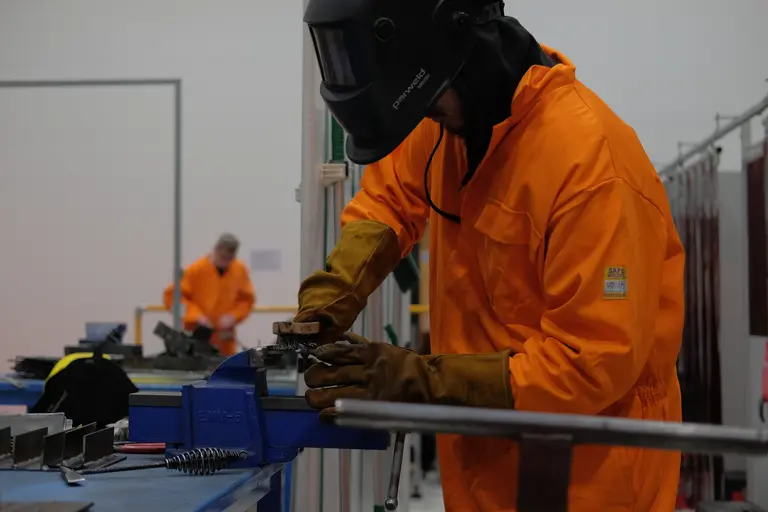Workers in orange jumpsuit welding with mask in factory.