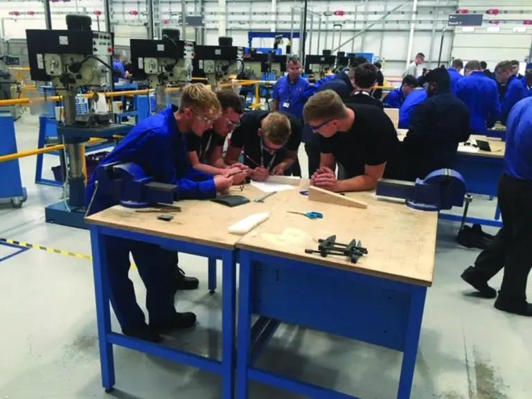 Several apprentices in blue uniforms work on tasks in a factory.