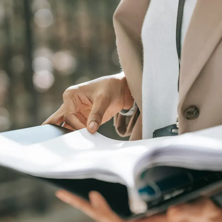 A person in a beige blazer holds a folder with an open document.